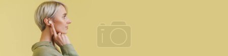 Téléchargez les photos : Agréable belle fille argentée posant dans des écouteurs sans fil isolés sur fond beige - en image libre de droit