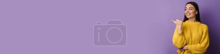 Téléchargez les photos : Heureuse belle fille souriante tout en pointant du doigt isolé sur fond violet - en image libre de droit