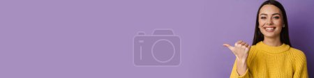 Photo for Happy nice girl smiling while pointing finger aside isolated over purple background - Royalty Free Image