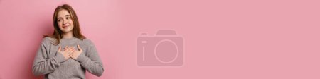 Photo for Ginger young happy woman smiling while holding hands on her chest isolated over pink background - Royalty Free Image