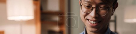 Téléchargez les photos : Sourire asiatique guy dans earphones jouer jeu vidéo sur téléphone mobile dans bureau - en image libre de droit