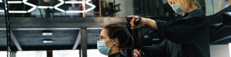 Téléchargez les photos : Jeune femme en masque facial faisant coiffure pour son client dans un salon de beauté - en image libre de droit