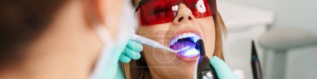 Europäische junge Frau sitzt im Behandlungsstuhl, während Zahnarzt ihre Zähne in Zahnklinik repariert