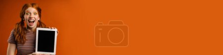 Téléchargez les photos : Gingembre excité femme avec des queues montrant comprimé pc isolé sur fond orange - en image libre de droit