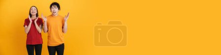 Téléchargez les photos : Jeune couple multiracial gesticulant et exprimant sa surprise devant la caméra isolée sur un mur jaune - en image libre de droit