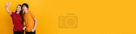 Photo for Smiling multiracial couple hugging while taking selfie on cellphone isolated over yellow wall - Royalty Free Image