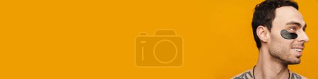 Téléchargez les photos : Gros plan d'un homme brunette d'âge moyen torse nu portant des patchs cosmétiques sur fond de mur jaune - en image libre de droit