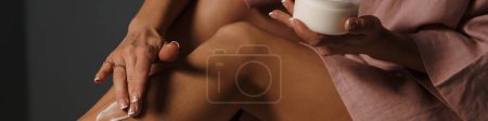 Téléchargez les photos : Femme blanche appliquant de la crème sur sa jambe dans le spa à l'intérieur - en image libre de droit