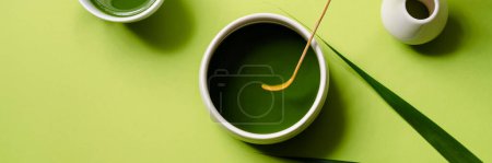 Photo for Overhead of a woman's hand mixing with a matcha spoon in a bowl standing next to a cup in a green studio - Royalty Free Image