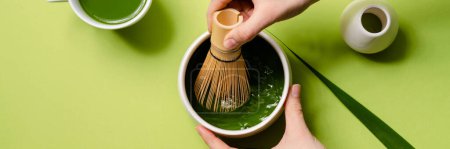 Photo for A close-up shot of a woman's hands mixing a matcha in a cup in a green studio - Royalty Free Image