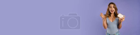 Téléchargez les photos : Jeune femme blanche se réjouissant et tenant téléphone cellulaire isolé sur fond violet - en image libre de droit