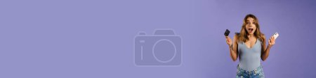 Téléchargez les photos : Jeune femme blanche tenant carte de crédit et téléphone cellulaire isolé sur fond violet - en image libre de droit