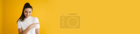 Téléchargez les photos : Jeune femme brune souriante et pointant du doigt isolé sur fond jaune - en image libre de droit