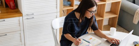 Photo for Focused woman doctor using earphone while working with laptop and papers at home, online consult - Royalty Free Image