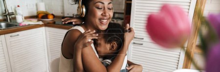 Foto de Mujer negra feliz con auriculares abrazando a su hijo mientras trabaja en casa - Imagen libre de derechos