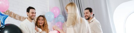 Photo for Young happy couple accepting gifts from her friend during gender reveal party indoors - Royalty Free Image