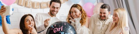 Photo for Young excited couple blowing up surprise balloon during gender reveal party indoors - Royalty Free Image