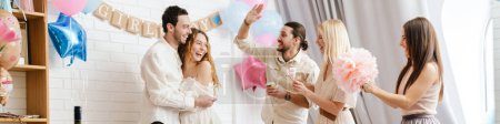 Photo for Young excited couple making fun with their friends during gender reveal party indoors - Royalty Free Image