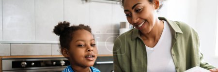 Photo for Black smiling woman drawing with her daughter at home kitchen - Royalty Free Image