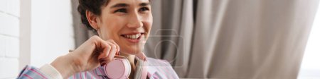 Foto de El retrato de una mujer sonriente con auriculares en el cuello mirando hacia otro lado mientras está sentada en la sala de luz - Imagen libre de derechos