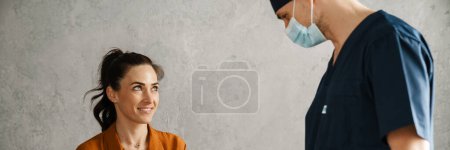 Photo for Woman patient and man doctor sitting in the cabinet during medical examination, doctor measuring temperature - Royalty Free Image