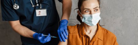 Foto de Mujer enferma con máscara médica recibiendo una vacuna sentada en un armario - Imagen libre de derechos