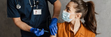 Foto de Mujer enferma con máscara médica recibiendo una vacuna sentada en un armario - Imagen libre de derechos