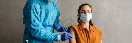 Photo for Sick woman in medical mask getting a vaccine shot sitting in a cabinet - Royalty Free Image