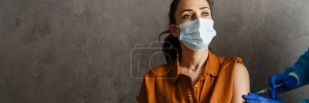 Photo for Woman patient wearing protective mask getting vaccinated from covid 19 by the doctor in his cabinet - Royalty Free Image
