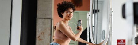 Téléchargez les photos : Souriant jeune femme blanche prenant une photo d'elle-même dans le miroir tout en étant assis sur un sol avec ordinateur portable - en image libre de droit