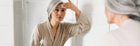 Foto de Mujer gris madura limpiando su cara con almohadilla de algodón en el baño en casa - Imagen libre de derechos