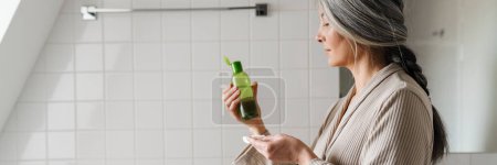 Foto de Mujer gris madura limpiando su cara con almohadilla de algodón en el baño en casa - Imagen libre de derechos