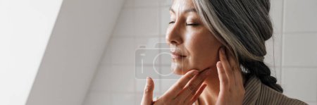 Foto de Mujer gris madura recibiendo masaje facial en el baño en casa - Imagen libre de derechos
