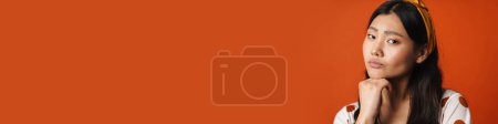 Téléchargez les photos : Jeune femme asiatique coûteuse en vêtements d'été debout sur fond orange, en regardant la caméra - en image libre de droit