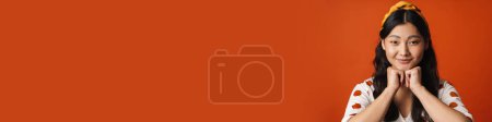 Téléchargez les photos : Souriant jeune femme asiatique en vêtements d'été debout sur fond orange, regardant la caméra - en image libre de droit