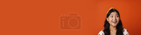 Téléchargez les photos : Souriant jeune femme asiatique en vêtements d'été debout sur fond orange, regardant de côté - en image libre de droit