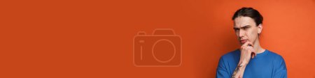 Téléchargez les photos : Jeune homme blanc avec boucle d'oreille fronçant les sourcils et regardant la caméra isolée sur fond orange - en image libre de droit