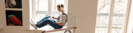 Photo for Young man in headphones using laptop while working on craft rug at home - Royalty Free Image