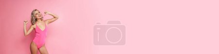 Photo for Portrait of a smiling blonde young woman wearing swimsuit standing over pink wall background, pointing fingers at herself - Royalty Free Image