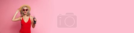 Photo for Happy young blonde woman in swimsuit and sunglasses holding fizzy drink bottle standing posing isolated over pink background - Royalty Free Image
