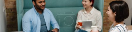 Téléchargez les photos : Trois collègues assis en pause café sur un canapé dans des tasses à café avec patron tenant un téléphone portable - en image libre de droit