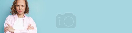 Téléchargez les photos : Jeune femme rousse fronçant les sourcils tout en posant avec les bras croisés isolé sur fond bleu - en image libre de droit