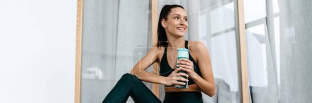Photo for White brunette woman smiling and drinking water while working out at home - Royalty Free Image