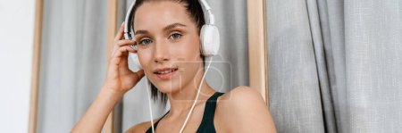 Foto de Mujer morena blanca sonriendo y escuchando música con auriculares en casa - Imagen libre de derechos