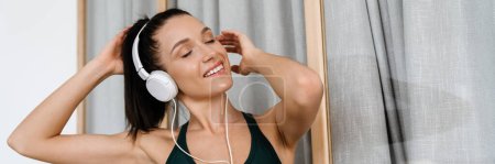 Photo for White brunette woman listening music with headphones while working out at home - Royalty Free Image