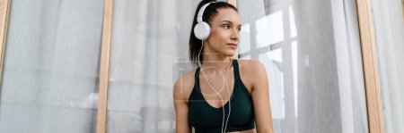 Foto de Mujer blanca escuchando música con auriculares y teléfono celular mientras hace ejercicio en casa - Imagen libre de derechos