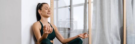 Photo for White brunette woman sitting and meditating after workout at home - Royalty Free Image