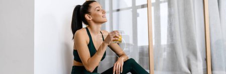 Photo for White brunette woman drinking juice and using laptop while sitting on floor at home - Royalty Free Image