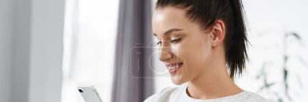 Photo for European smiling woman using mobile phone while sitting on couch at home - Royalty Free Image