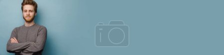 Téléchargez les photos : Blanc gingembre homme regardant caméra tout en posant avec les bras croisés isolé sur fond bleu - en image libre de droit